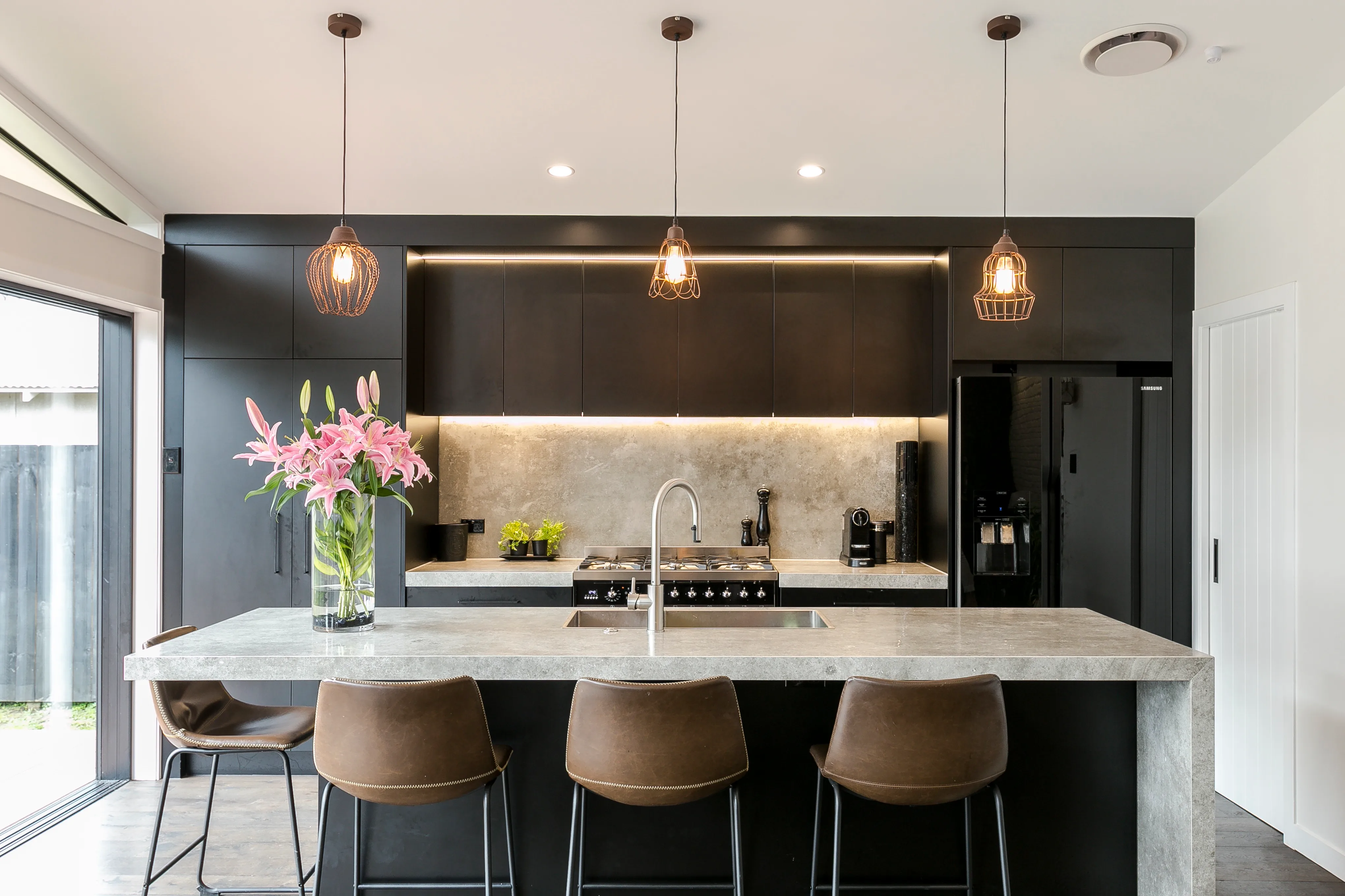 Hazelmere house – kitchen with black cabinetry, copper pendant lights and marble-look splashback
