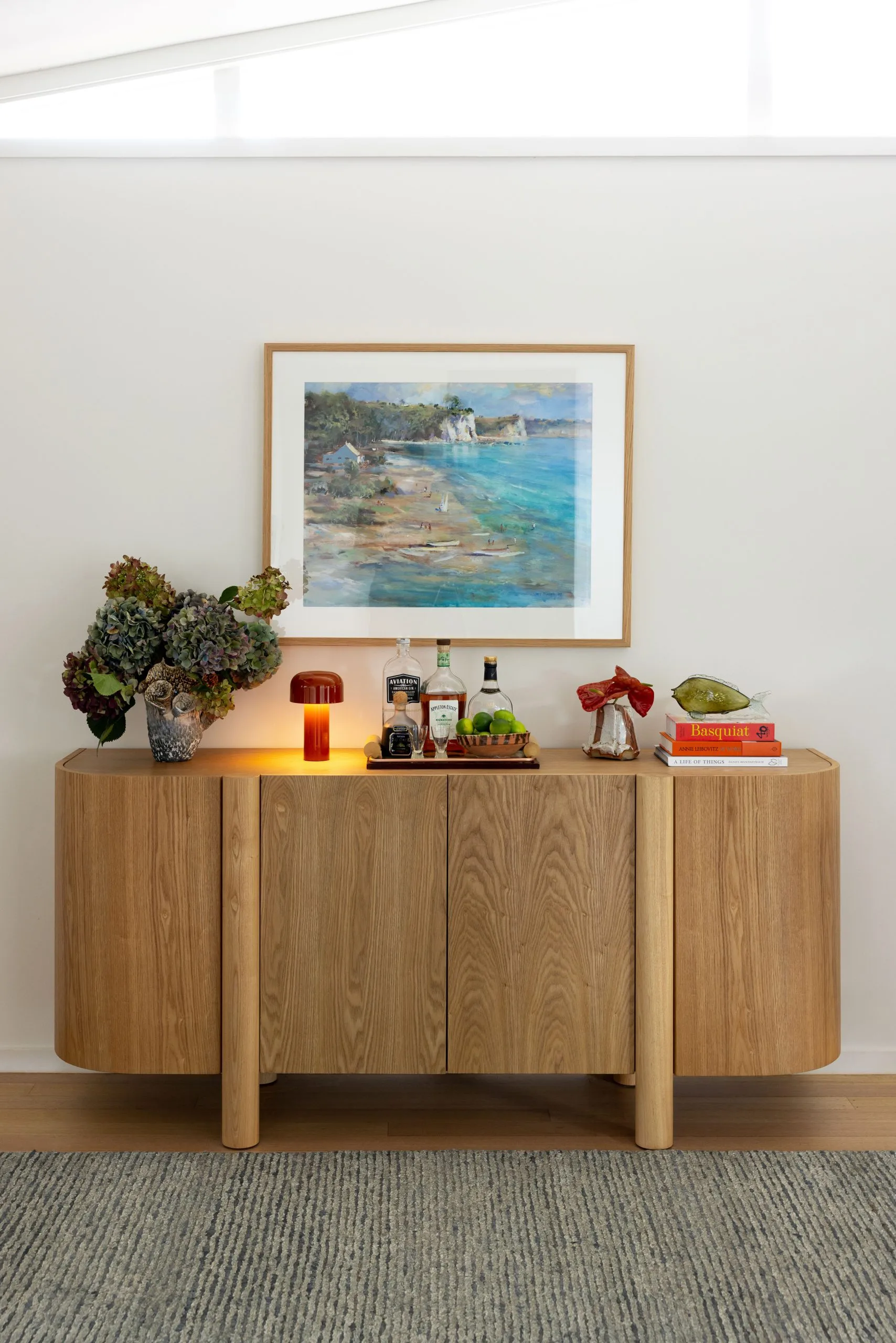 Deep Creek – sideboard with a framed coastal painting and a bar tray of spirits and glassware
