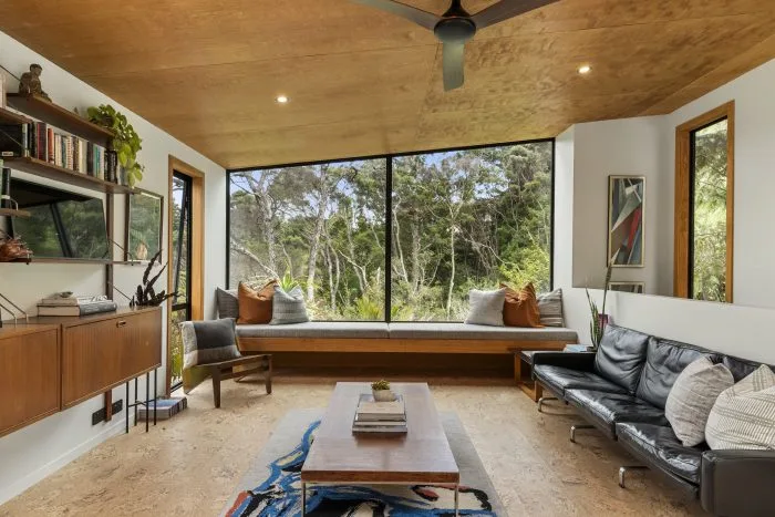 Kauri – living room with a built-in window seat, black leather sofa and bookshelves